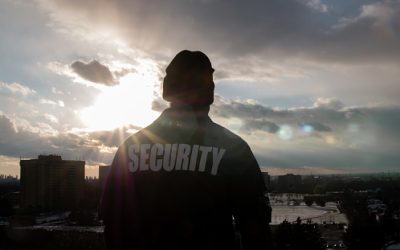 A black male security guard in uniform watching over the street from the high floor.